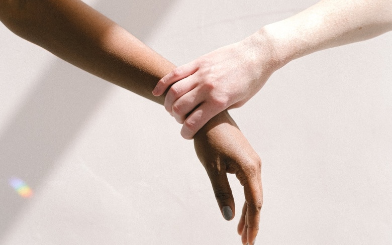 Main de femme blonde tenant la main d une femme noire - comment attenuer les rides sur les mains| Dr Santini Paris 16